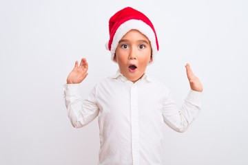 Sticker - Beautiful kid boy wearing Christmas Santa hat standing over isolated white background afraid and shocked with surprise expression, fear and excited face.