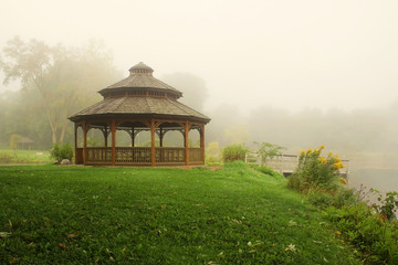 Wall Mural - early autumn foggy morning landscape. scenic view with wooden gazebo on a green grass lawn near the 