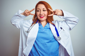 Poster - Young redhead doctor woman using stethoscope over white isolated background Doing peace symbol with fingers over face, smiling cheerful showing victory