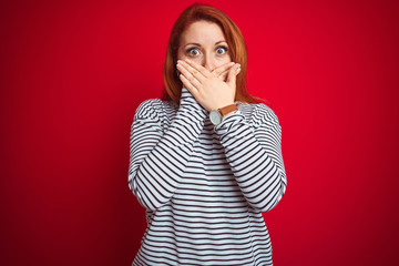 Wall Mural - Young redhead woman wearing strapes navy shirt standing over red isolated background shocked covering mouth with hands for mistake. Secret concept.