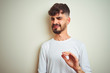 © Krakenimages.com - Young man with tattoo wearing t-shirt standing over isolated white background disgusted expression, displeased and fearful doing disgust face because aversion reaction. With hands raised