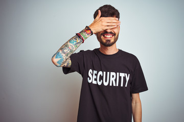 Sticker - Young safeguard man with tattoo wering security uniform over isolated white background smiling and laughing with hand on face covering eyes for surprise. Blind concept.