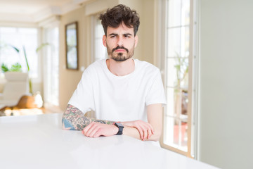 Poster - Young man wearing casual t-shirt sitting on white table skeptic and nervous, frowning upset because of problem. Negative person.