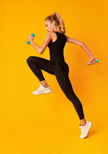 Sporty Millennial Girl Jumping With Dumbbells On Yellow Background, Studio