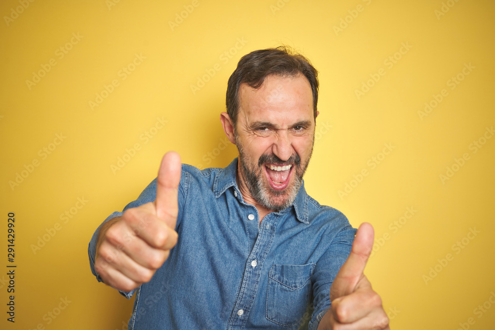 Handsome middle age senior man with grey hair over isolated yellow background approving doing positive gesture with hand, thumbs up smiling and happy for success. Winner gesture.