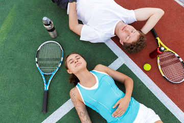 Image of fitness man and woman lying on court while playing tennis