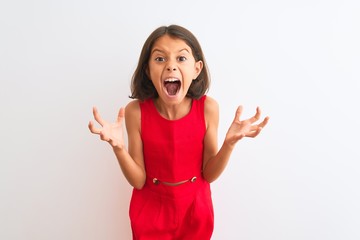 Young beautiful child girl wearing red casual dress standing over isolated white background crazy and mad shouting and yelling with aggressive expression and arms raised. Frustration concept.