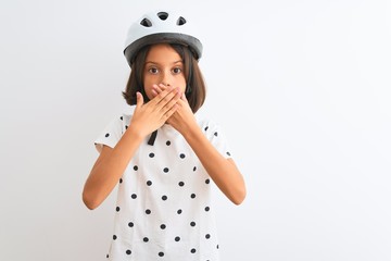 Sticker - Beautiful child girl wearing security bike helmet standing over isolated white background shocked covering mouth with hands for mistake. Secret concept.