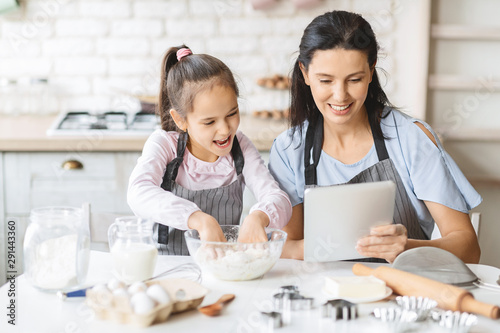 Cuadros en Lienzo Mother and daughter using digital tablet in kitchen, looking recipe