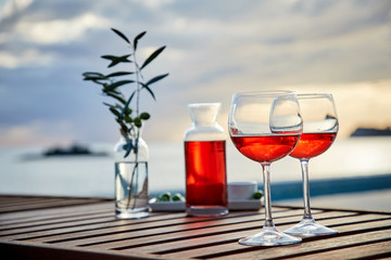 two glasses of rose wine with  olives against blue water on a pier..