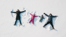 Family Making A Snow Angel. Aerial View. Mother And Father And Chilren Making A Snow Angel