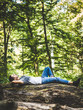 Young guy resting on a trunk in the forest and enjoying the pure air
