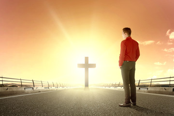 Rear view of Asian businessman looking at Christian cross at the end of the asphalt road