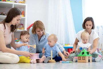  Group of workers with babies in nursery or kindergarten. Moms playing with kids in creche