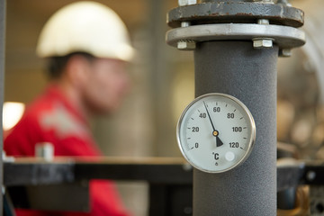 Central heating network. Thermometer on the hot water supply pipe to the heating system. Technician wearing red jacket with white helmet blurred in background. Start of the heating season.