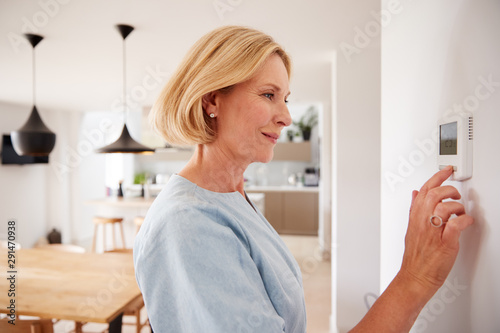 Fotografía Close Up Of Mature Woman Adjusting Central Heating Temperature At Home On Thermo
