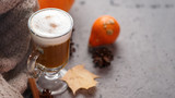 Fototapeta Mapy - Autumn pumpkin latte glass. A warming drink and a knitted scarf on the gray table. Thanksgiving day