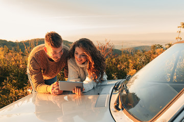 Beautiful couple on road trip, they are taking a break from driving and looking for direction on tablet.