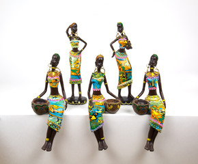 Figurines of ceramics. African American women painted in bright national outfits sitting standing isolated on a white background. African motif. National traditions style. Idea design concept.