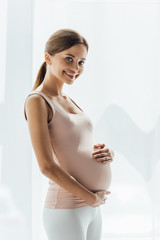 Wall Mural - attractive pregnant young woman touching belly and looking at camera