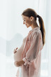side view of happy pregnant woman smiling and touching belly