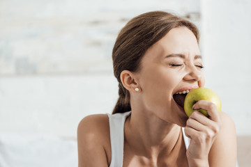 attractive young woman eating green apple with closed eyes