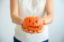 A Woman In A White Blouse Holds A Pumpkin For Halloween. Close-up Of Female Hands With A Lantern Jack On A White Background On The Eve Of All Saints. Foreground. Trick Or Treat. Scary Grimace.