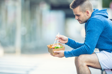 Young man having lunch asian food from box of recycled paper