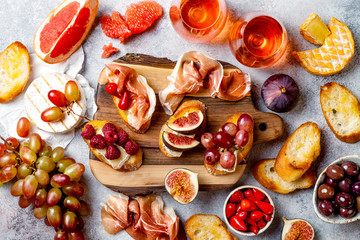  Appetizers, antipasti snacks and rose wine in glasses. Bruschetta or authentic traditional spanish tapas set, cheese and meat platter over grey concrete background. Top view