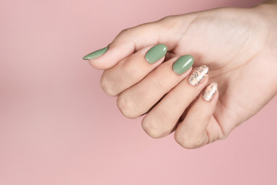 Closeup top view of beautiful trendy manicured fingernails painted in two colors: green and pink with silver stamping design. Female hand isolated on pink pastel background. Horizontal color photo.
