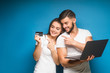 © Тарас Нагирняк - Happy young men and woman  holding laptop computer while standing with credit card and celebrating isolated over blue background. Online shopping.