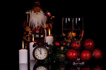 Wall Mural - Two wine glasses with champagne, Santa Clause, clock and christmas ornaments on a black background with reflection