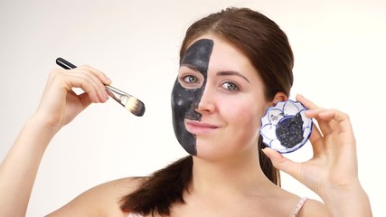 Wall Mural - Woman applying with brush clay carbo detox black mask to her face, on white. Girl taking care of oily skin complexion. Beauty treatment. Skincare