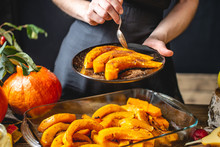 Woman Chef Holding Slices Of Baked Orange Pumpkin With Honey And Cinnamon. Autumn Food In A Cozy Kitchen. Close Up