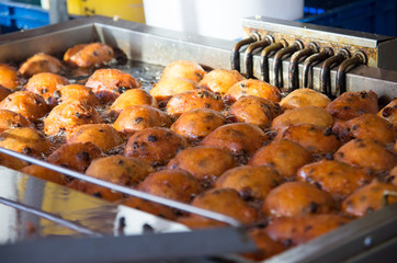 Close up of oliebollen with currants that are baking in a professional frying pan.