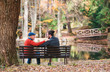Rear view of senior father and his son sitting on bench by lake in nature, talking.