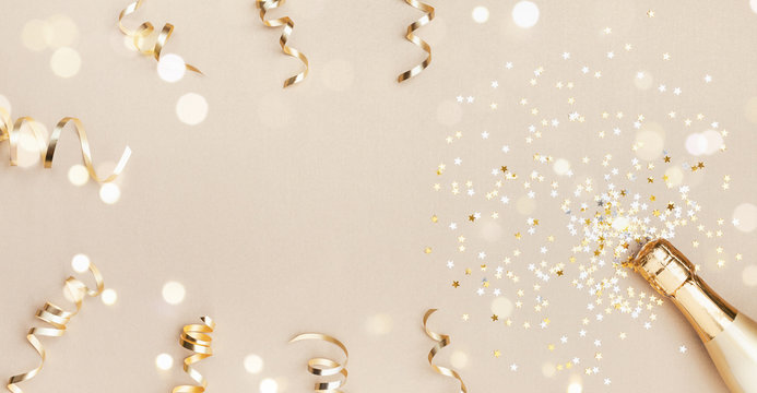Champagne bottle with confetti stars, bokeh decoration and party streamers on golden background. Christmas, birthday or wedding concept. Flat lay.