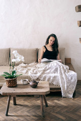 Wall Mural - Woman resting at home, reading book, sitting on sofa