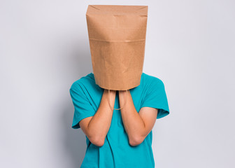 Unhappy teen boy with paper bag over head covering face with hands while crying. Upset teenager cover head with bag posing in studio. Child crying, not showing his tears.