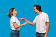 © ianachyrva - Couple of a young blond woman and brunet bearded man with mustaches in white t-shirts and blue jeans quarreling standing isolated over blue background.