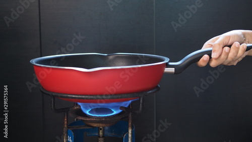 Fotomural hand holding red frying pan on retro and old rustic gas stove with flame on stove top for cooking