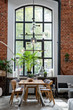 Bright industrial interior of loft apartment with big window. Dining room with bricky wall and modern table and chairs. Vertical.