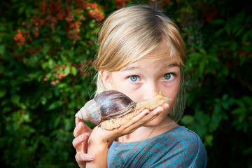 portrait of preteen adorable child girl playing with her pet giant african snail (achatina fulica). 