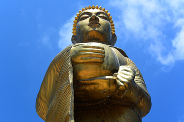 Golden statue of a standing Buddha against a blue sky