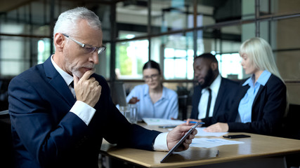 Wall Mural - Mature businessman thinking of decision looking tablet, managers discussing plan