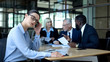 © motortion - Irritated company worker feeling headache, rubbing temples, colleagues arguing