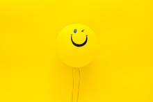 Happiness Emotion. Yellow Balloon With Smile On Yellow Background Top View Copy Space