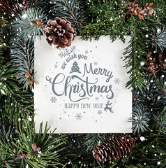 Wall Mural - Merry Christmas and New Year Text on paper card note over holiday background with fir branches, snow and pine cones. Xmas and New Year theme. Flat lay, top view
