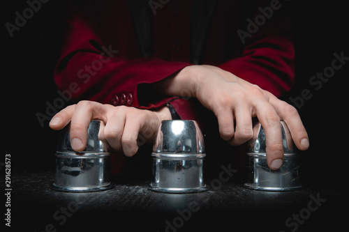Fotomural Magician shows shell game of thimbles with circles and ball, black background