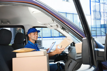 Canvas Print - Young courier with clipboard and parcels in delivery car